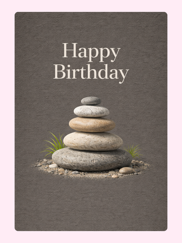 A tranquil birthday card featuring a stack of smooth stones arranged in a balanced formation with subtle grass accents, set against a muted gray background. The text "Happy Birthday" is elegantly displayed in white font.