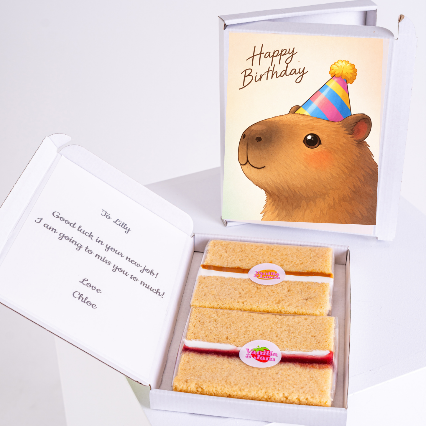Capybara with a striped birthday hat, holding a gift, with a personalized message and slices of cake inside a box.
