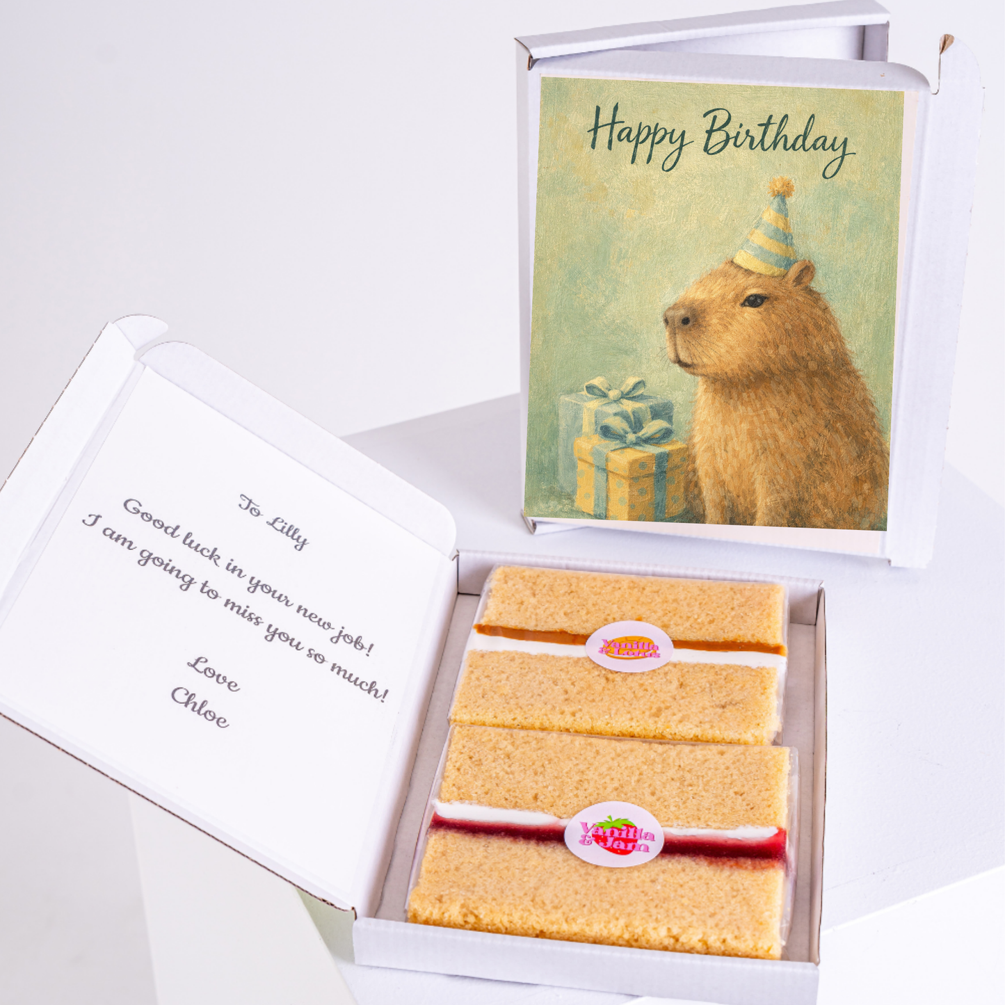 A capybara wearing a birthday hat, with a "Happy Birthday" card and two slices of cake in a box, alongside a personalized message.