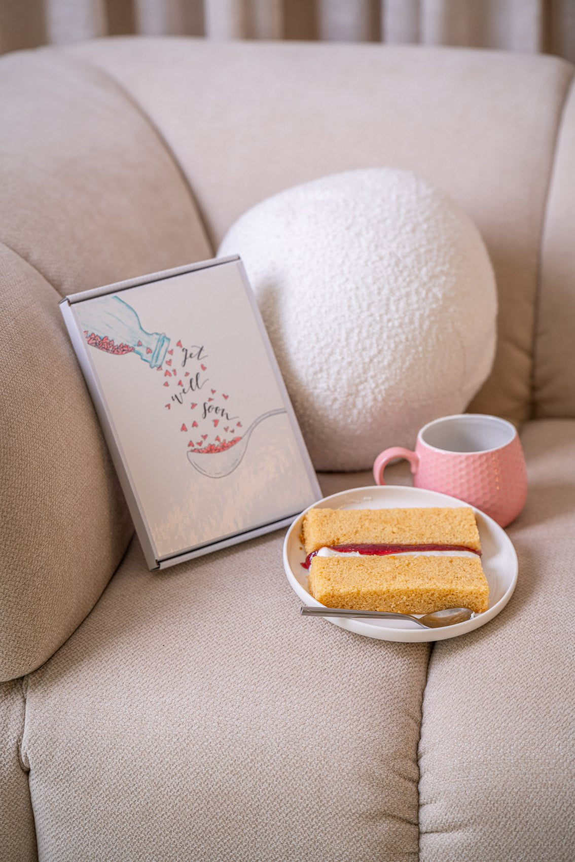 A cake card and cake slices beside a pink cup on a sofa