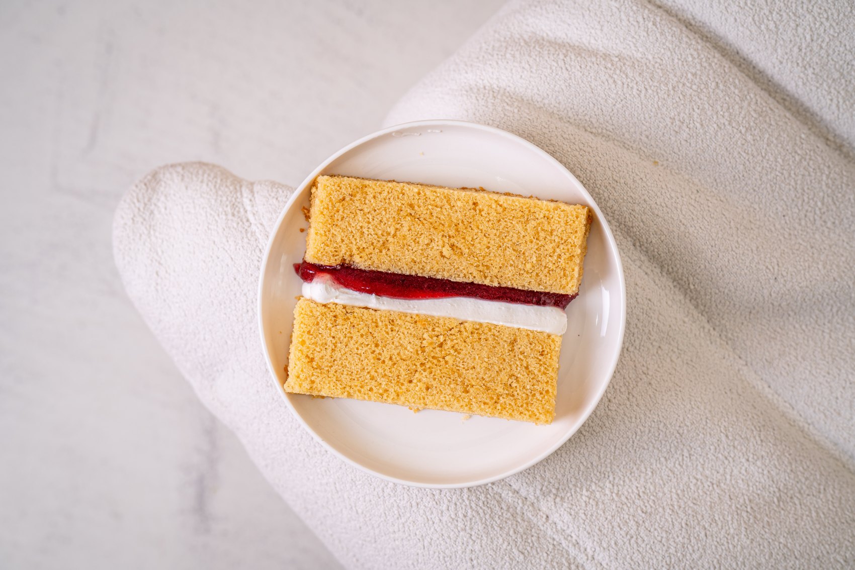 A vanilla sponge cake slice with jam and cream filling on a plate